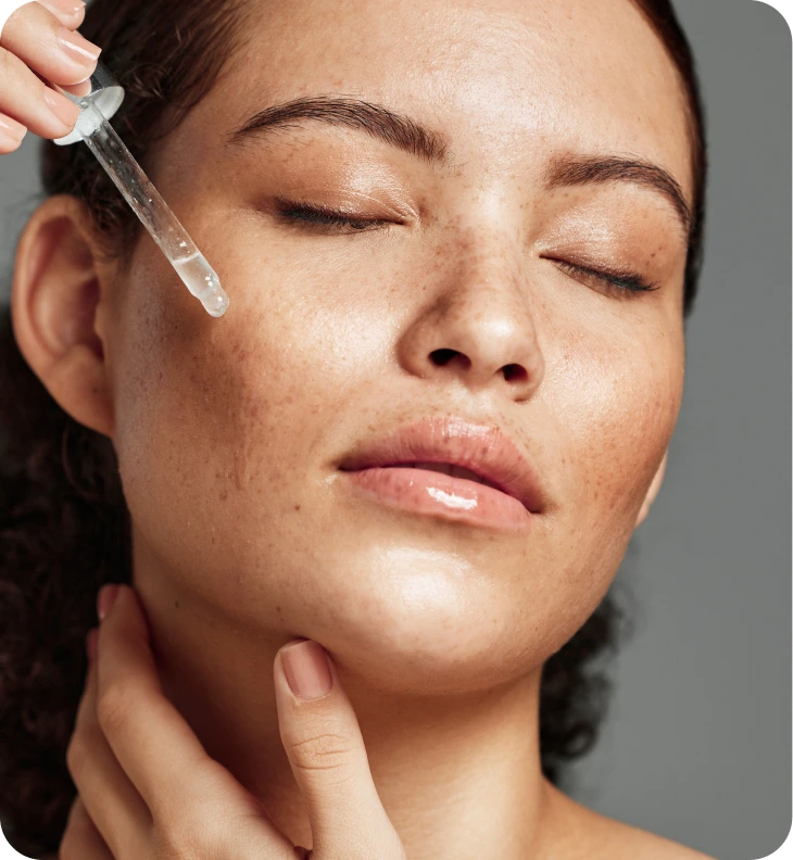 Woman applying clear serum to her cheek with a glass dropper